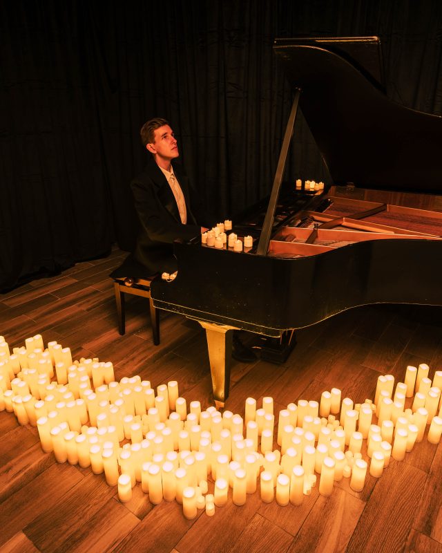 Pianista przy fortepianie, przed nim rozstawione dziesiątki świec